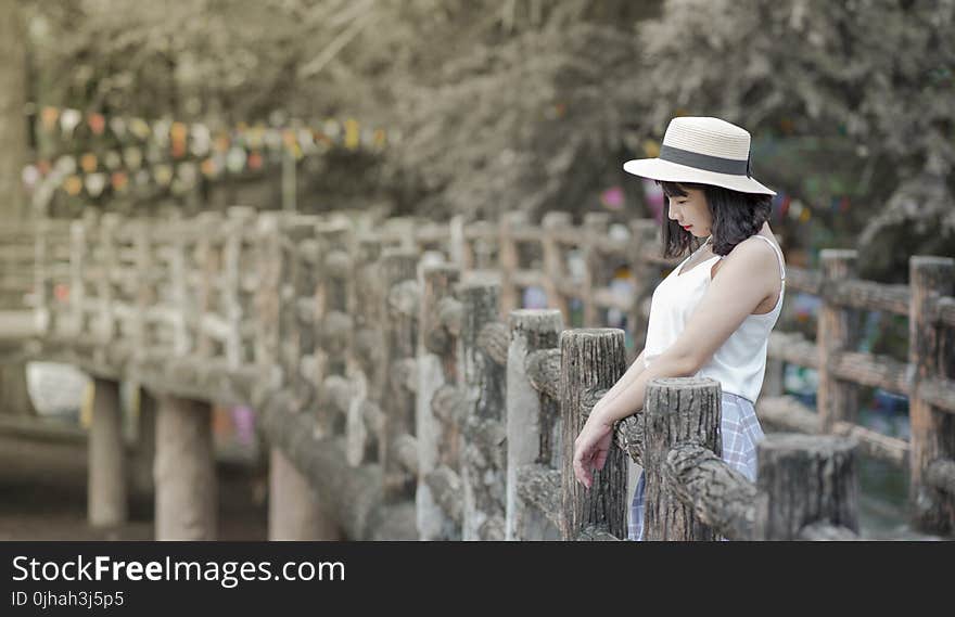 Woman Wearing White Tank Top and White Hat Standing on a Boardwalk