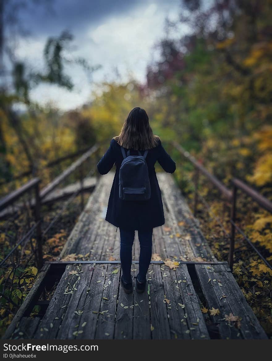 Selective Focus Photography of Woman Wearing Black Overcoat Standing on Wooden Bridge