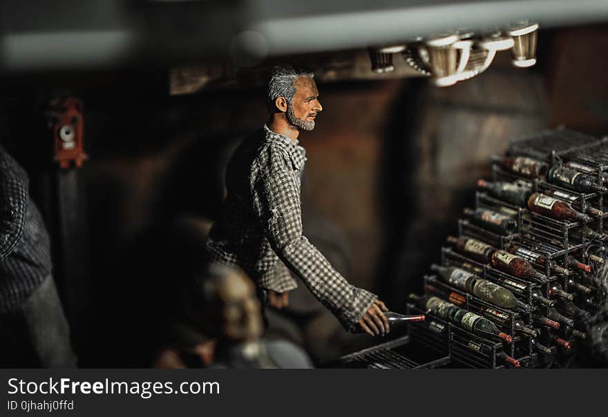 Selective Focus Photography of Male Doll Holding Bottle Near Bottle Rack