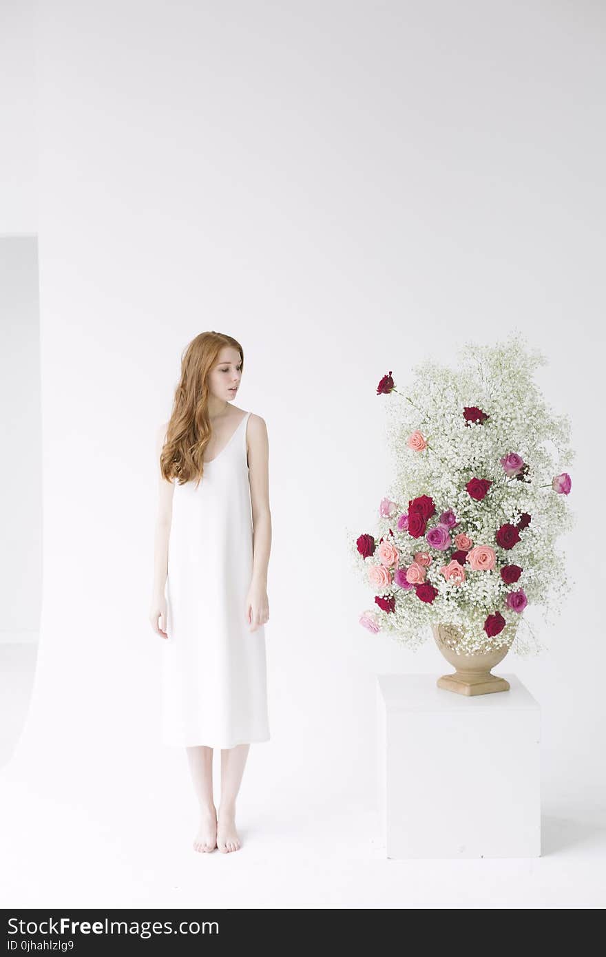 Woman in White Spaghetti Strap Midi Dress Standing Beside Table With Flowers