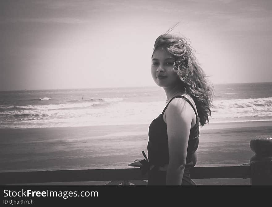 Grayscale Photo of Woman Wearing Tank Top Standing Near Seashore