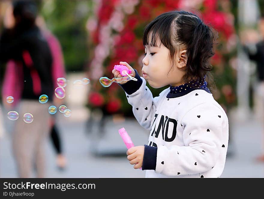 Toddler Girl Wearing White and Black Sweater Holding Plastic Bottle of Bubbles at Daytime