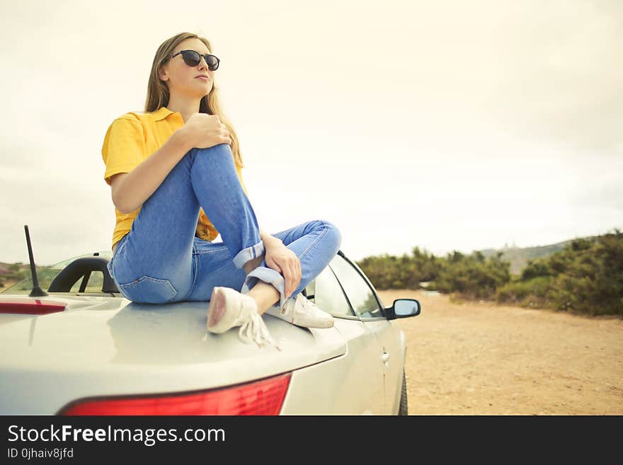 Woman Wears Yellow Shirt and Blue Denim Jeans Sits on Silver Car