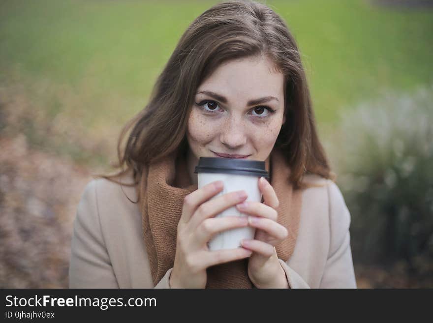 Woman in Brown Top and Scarf Holding a White and Black Travel Cup Outside