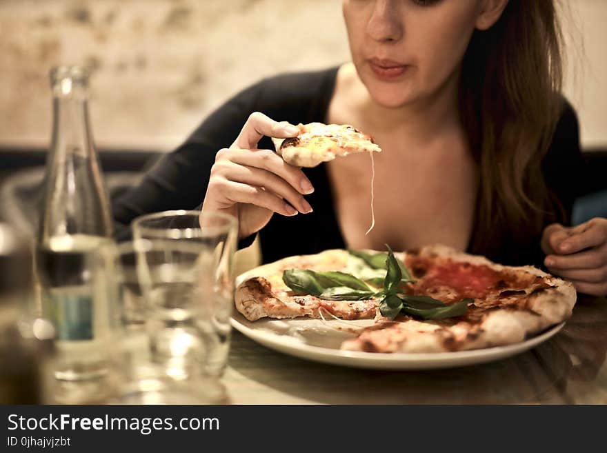 Woman Holds Sliced Pizza Seats by Table With Glass