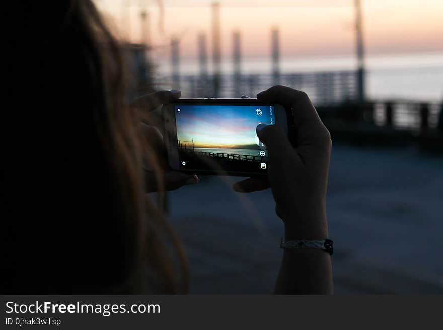 Brown Haired Woman Taking a Photo of Sunset