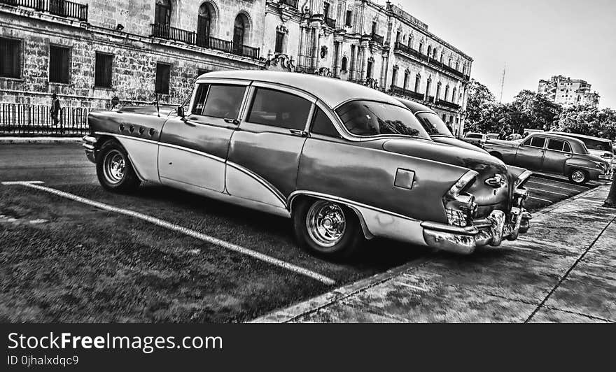 Greyscale Photo of Vintage Car Parked Beside Building