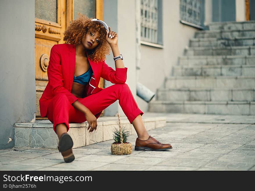 Woman Wearing Red Blazer and Pants Sitting on Marble Ground