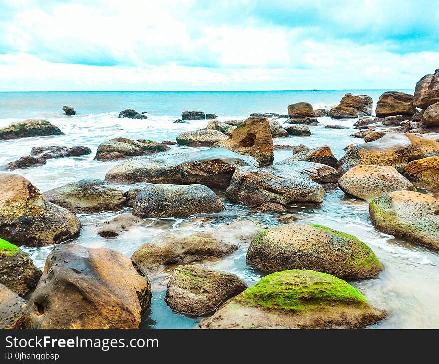 Landscape Photography of Rocks With Moss Surrounded by Body of Water