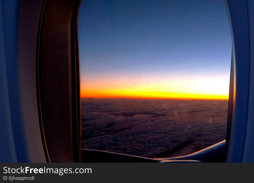 Photo of Airplane Window With View of Clouds and Golden Hour