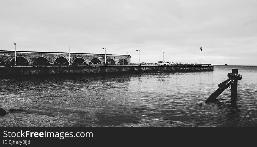 Grayscale Photo of Body of Water Near White Concrete Wall