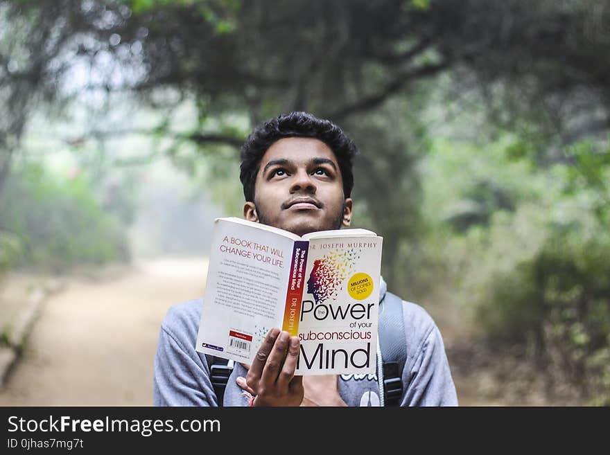 Man in Grey Shirt Holding Opened Book Looking Upward