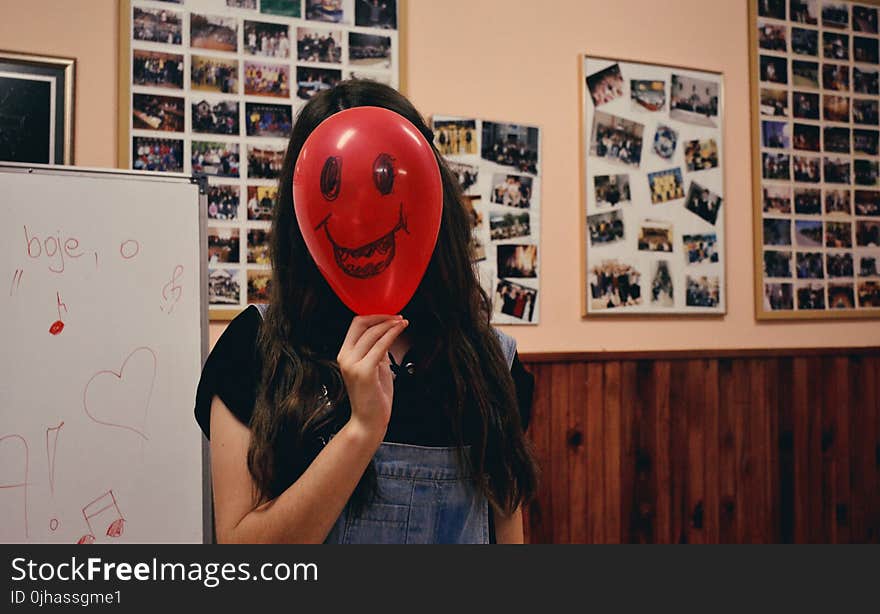 Woman Holding Red Balloon on Her Face Photo Inside Classroom