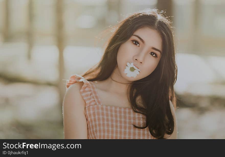 Woman Wearing Orange Sleeveless Dress Bites White Petaled Flower