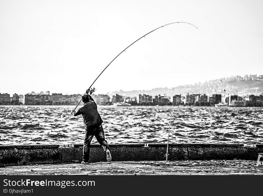 Grayscale Photography of Man Holding a Fishing Rod Near Body of Water