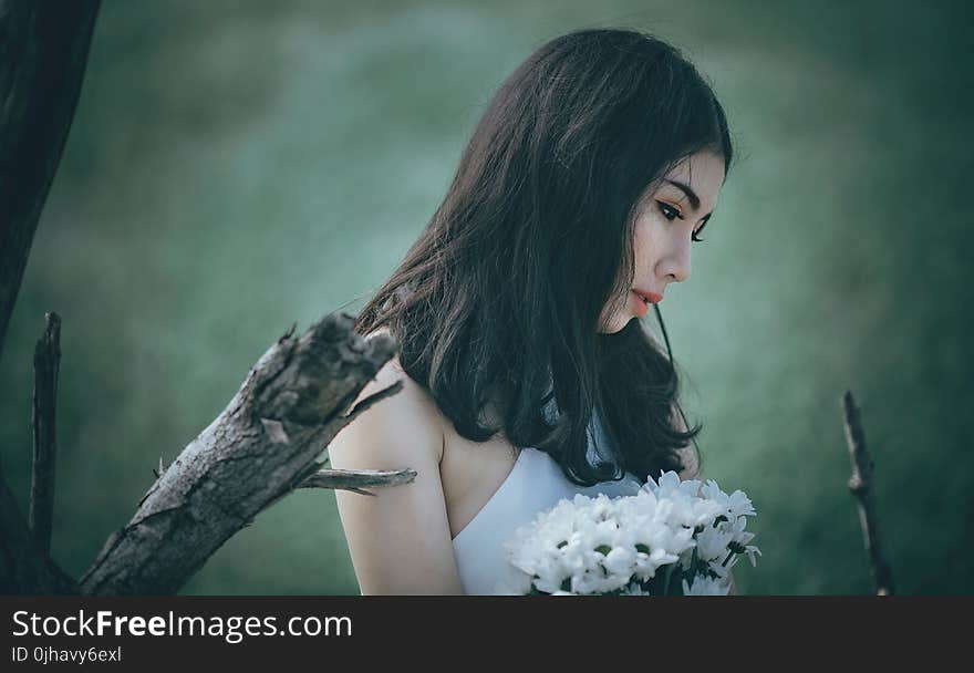 Woman in White Top Holding Bouquet of White Petaled Flowers While Looking Down