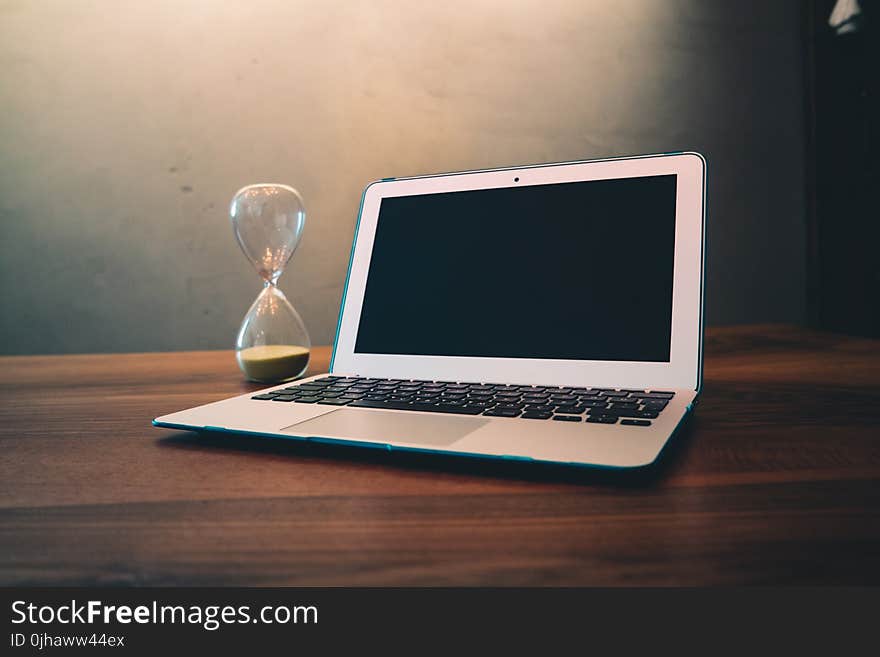 Computer Laptop Beside Hour Glass on Brown Wooden Surface