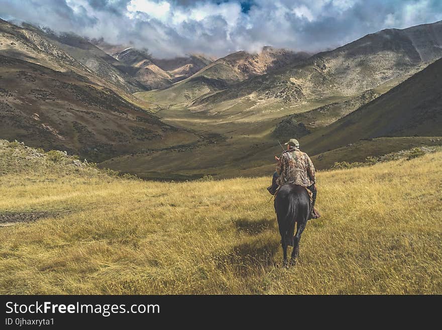 Man Riding Horse on Grass Near Mountains