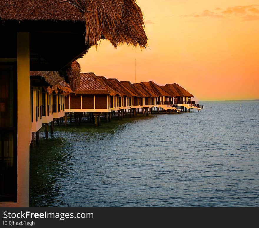 Architectural Photography of Brown Stilt Houses on Top of Sea Under Orange Sky