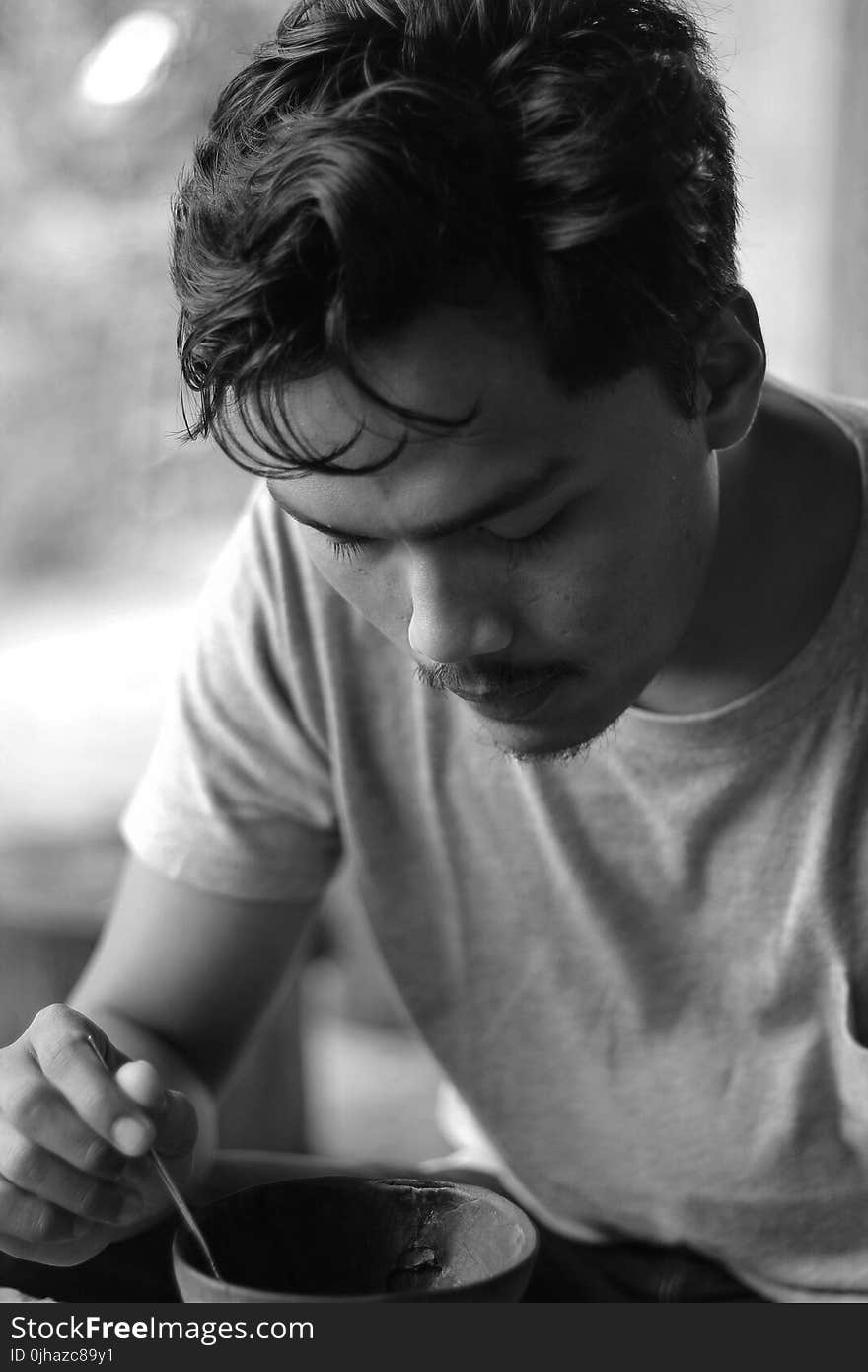 Gray Scale Photo of Man Holding Bowl and Spoon