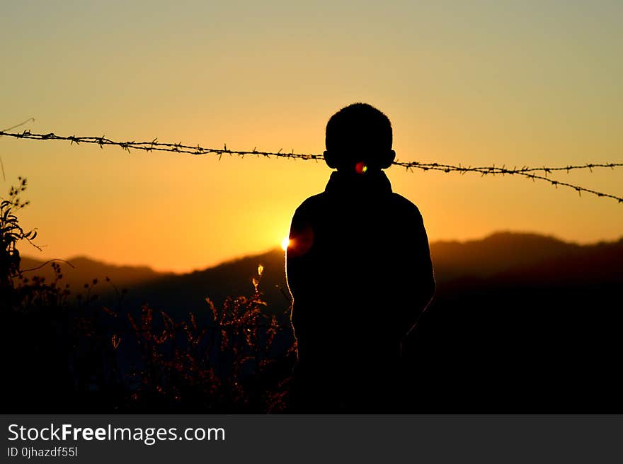 Silhouette of Boy Standing Near Barbed Wire Fence during Golden Hour