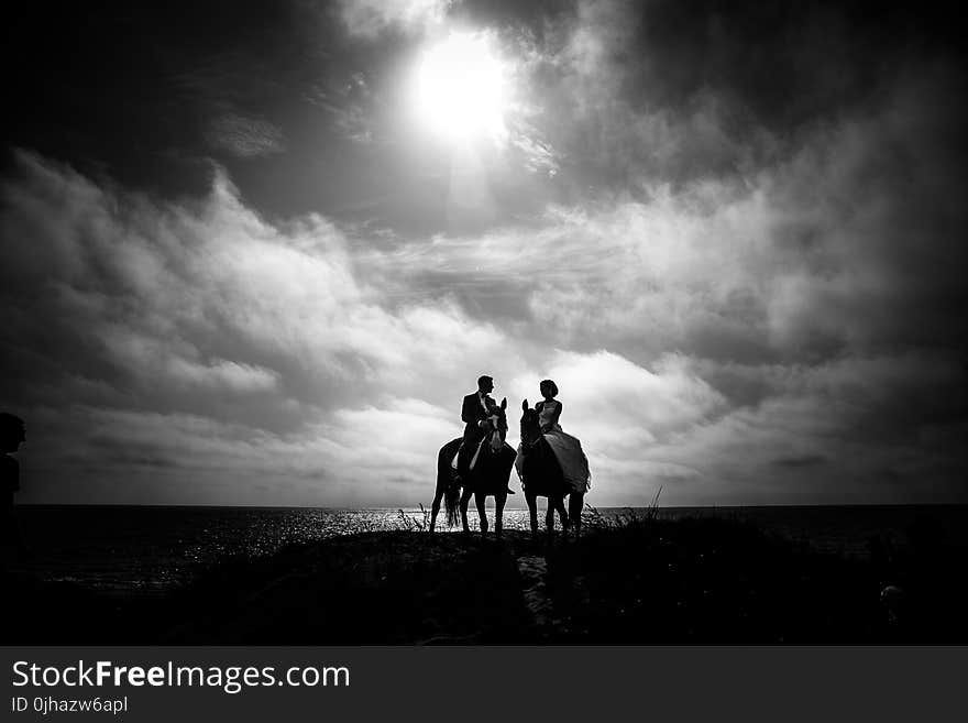 Grayscale Photography of Couple Riding on Horse With Body of Water and Sky As Background