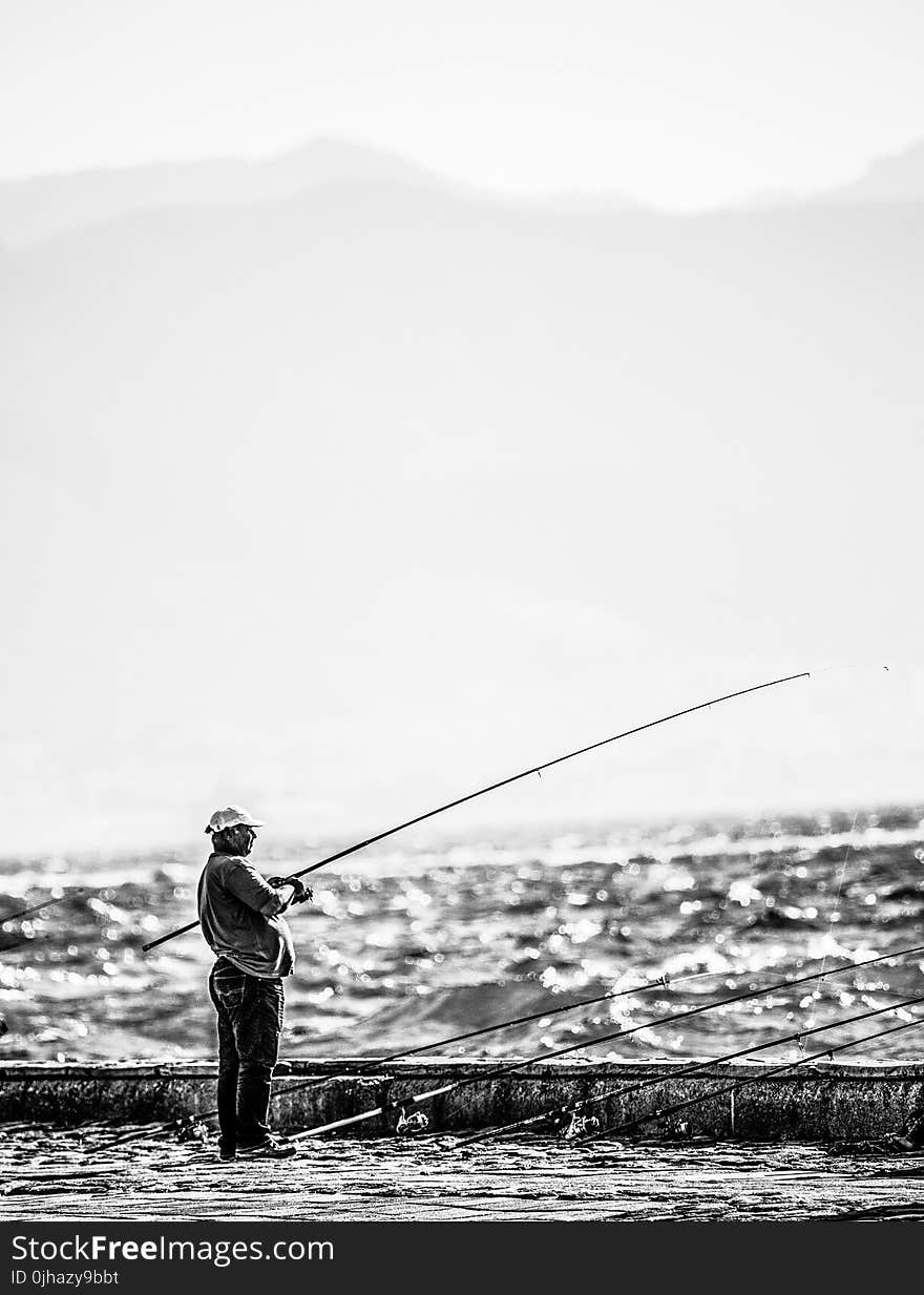 Man Standing Near Seashore Holding Fishing Rod on Grayscale Photography