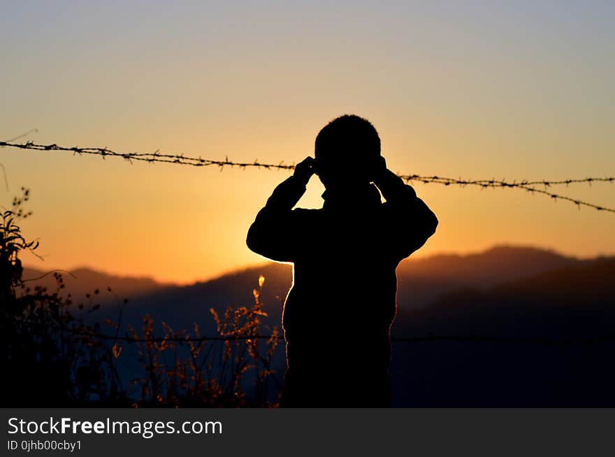 Silhouette of Boy Standing Near Barbed Wire