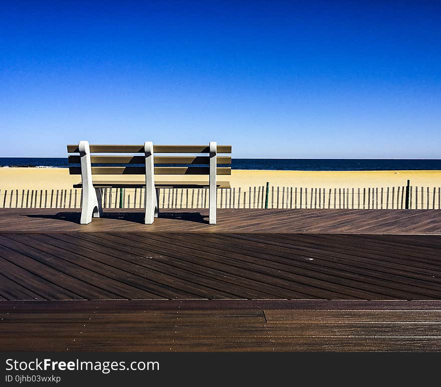 Brown-and-white Wooden Bench Facing Body of Water Under Clear Blue Sky