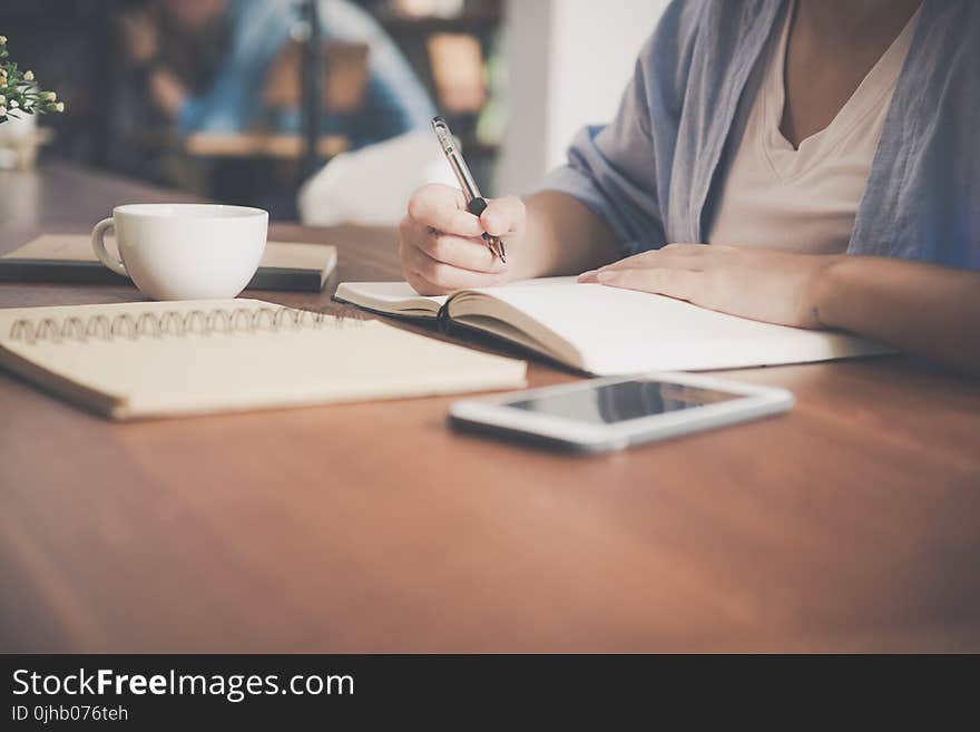 Woman Writing on a Notebook Beside Teacup and Tablet Computer