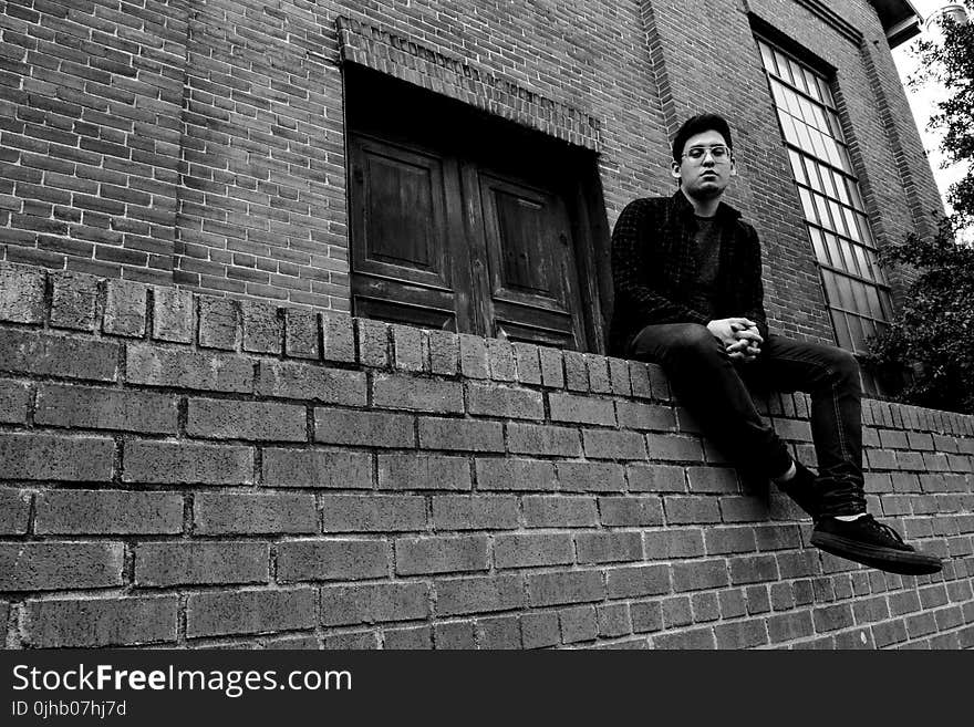 Grayscale Photography of Man Sitting on Brick Fence