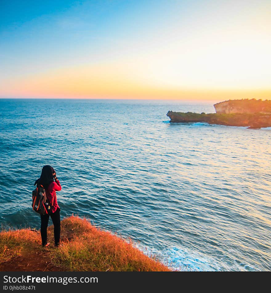 Woman in Red Shirt Wearing Gray and Pink Backpack Beside Body of Water