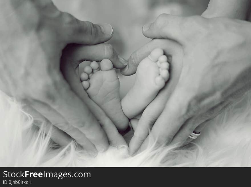 Grayscale Photo of Baby Feet With Father and Mother Hands in Heart Signs