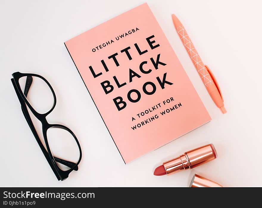 Little Black Book Surrounded With Pink Click Pen, Red Lipstick, and Black Wayfarer Eyeglasses