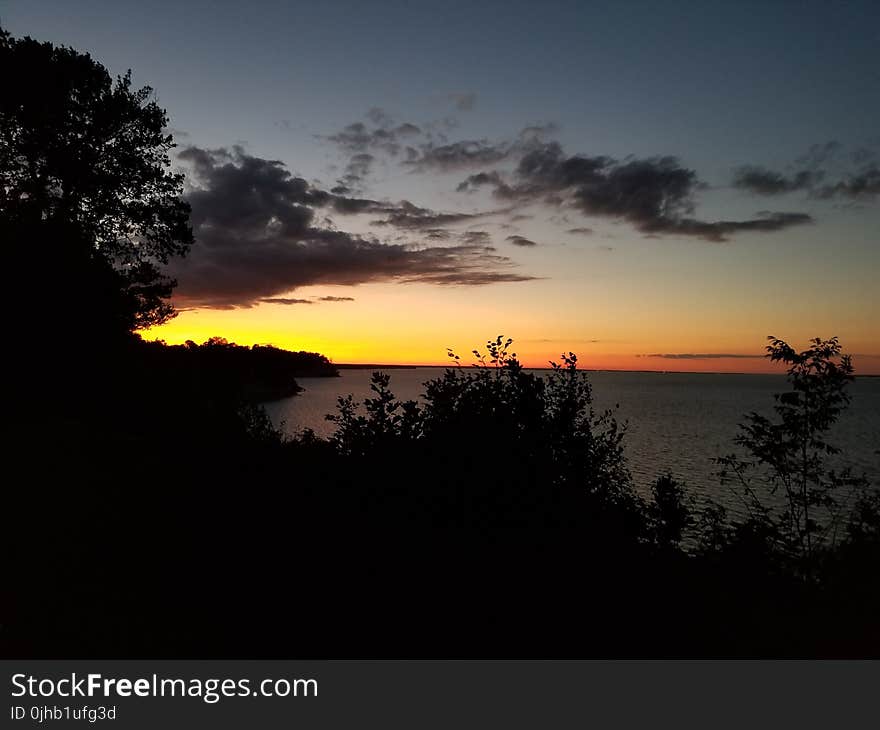 Body of Water Near Trees Under Orange Sunset