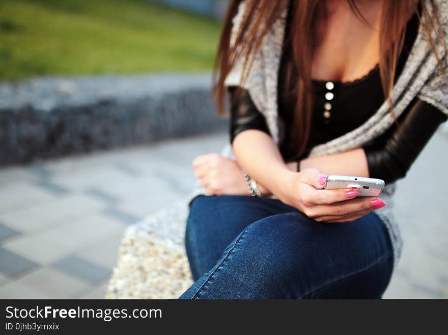 Woman in Black Elbow Sleeve Shirt and Blue Denim Jeans Sitting on the Grey Rock during Daytime