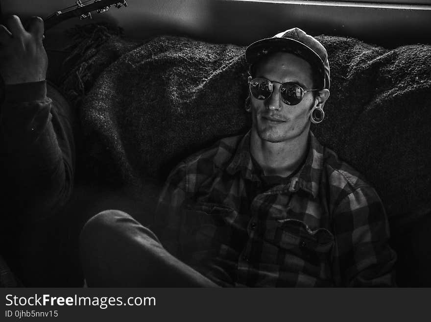 Grayscale Photo of Man Wearing Snapback Cap and Plaid Dress Shirt Sitting on Couch