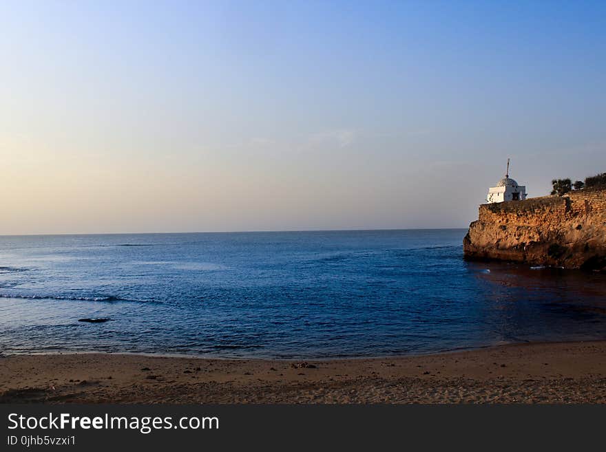 White Lighthouse Near Sea Under Blue Sky