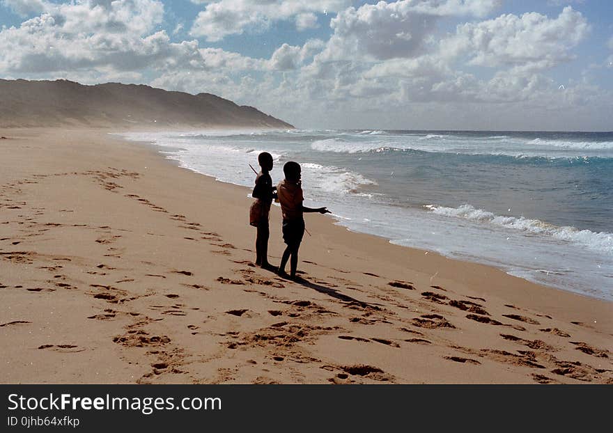 Two Children Stands on Shore Near Ocean at Daytime