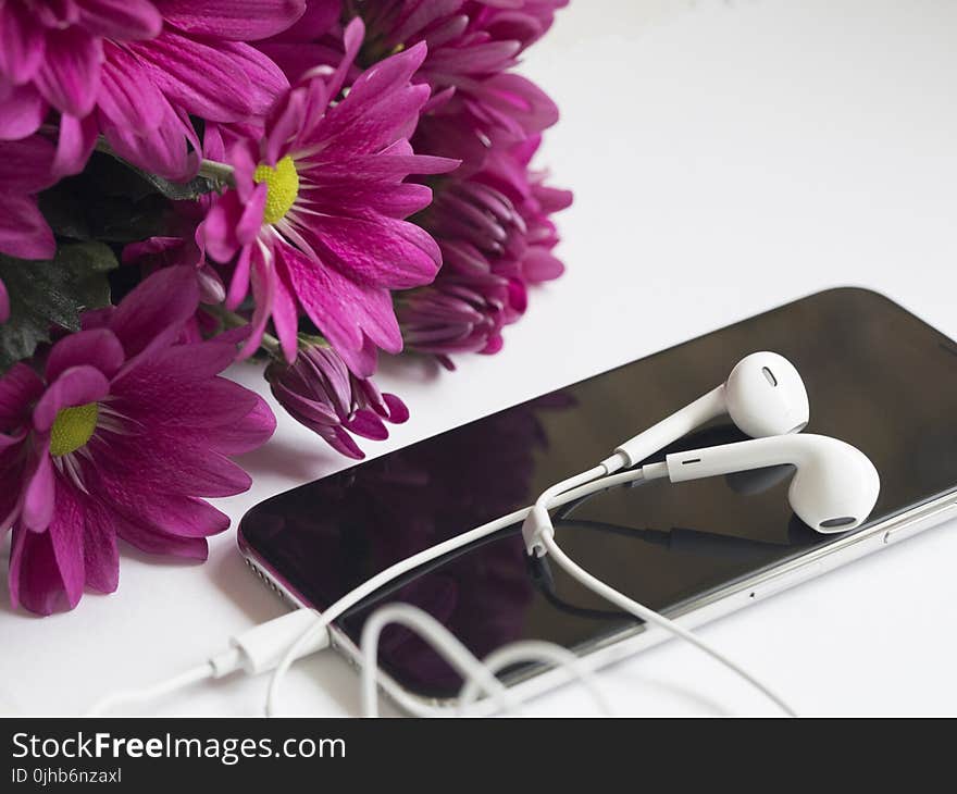 Close-Up Photography of Earphones on Top of Iphone 6 Near Flowers