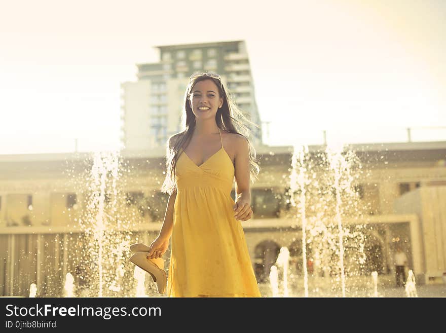 Woman Wears Yellow Spaghetti Strap Dress Stands Near Water Fountain