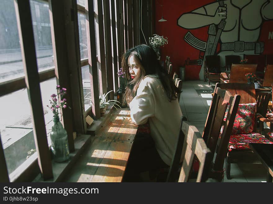 Woman Sitting on Chair Leaning on Table and on Facing Window