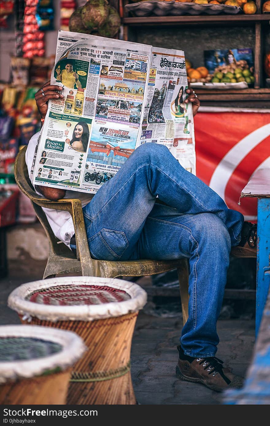 Man Sitting on Plastic Armchair Reading Newspaper