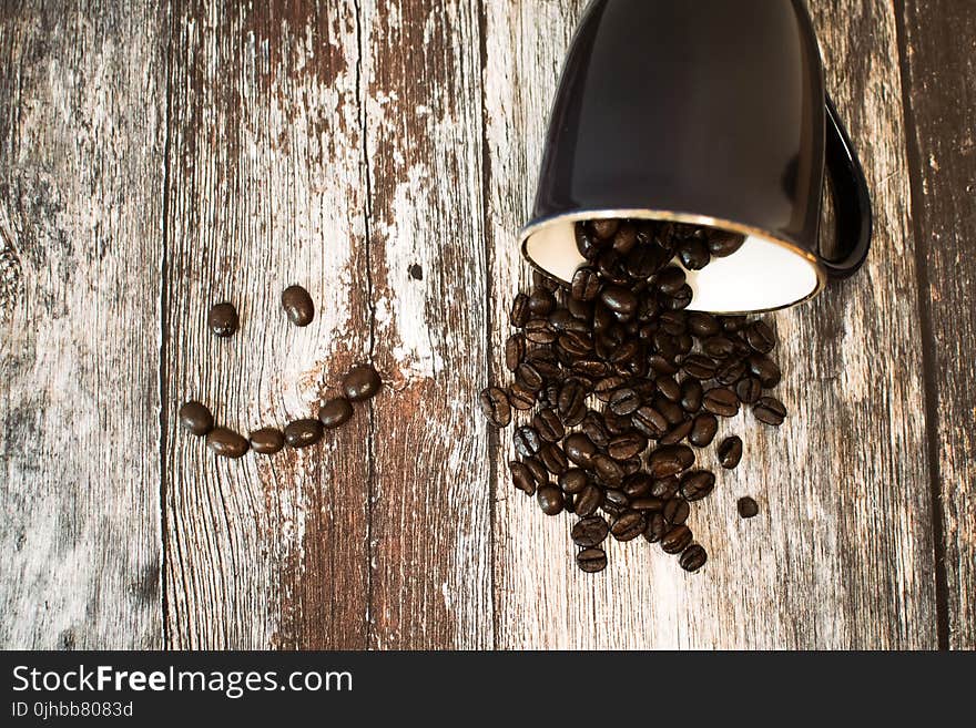 Black Ceramic Cup With Coffee Beans All on Brown Wooden Surface