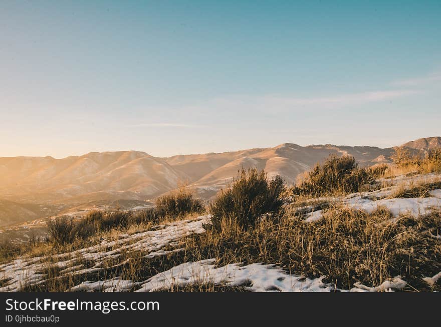 Green and Brown Grass Covered With Snow Overlooking Brown Hills and Mountains Under Clear Blue Sky at Daytime