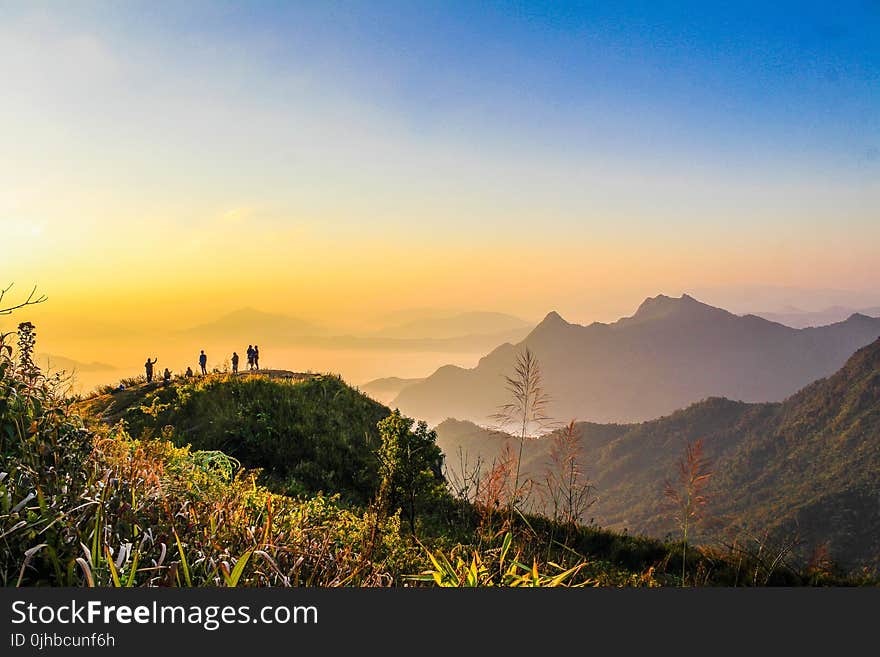 Photo of People Standing on Top of Mountain Near Grasses Facing Mountains during Golden Hours