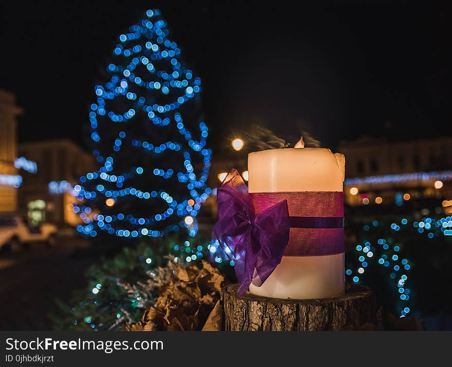 White Pillar Candle on the Log in a Distance of Blue Led Light Christmas Tree