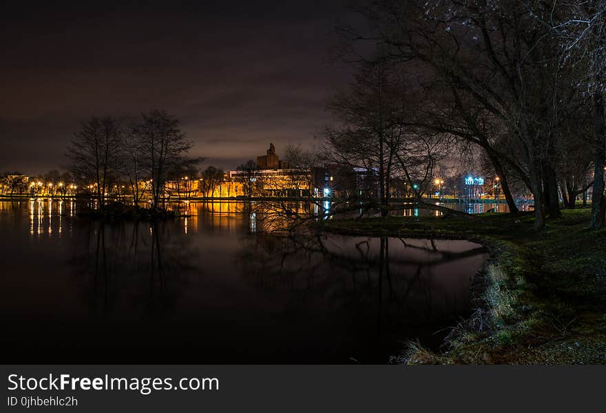 Still Body of Water Next to Lighted Beige Buildings during Nighttime