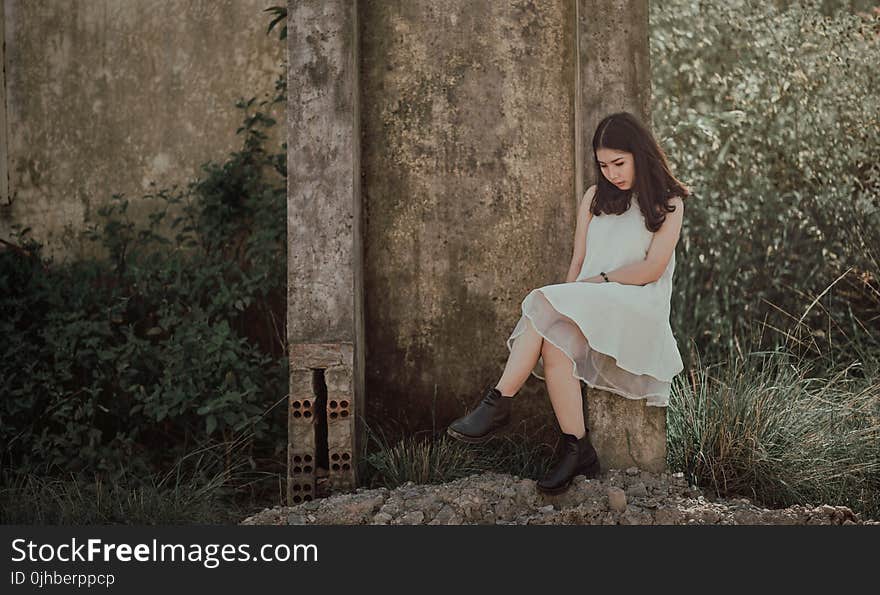 Woman Sitting on Slab Near Brown Wall