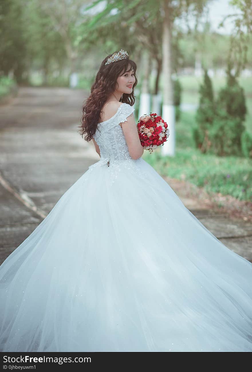 Woman in White Wedding Dress Holding Red Bouquet